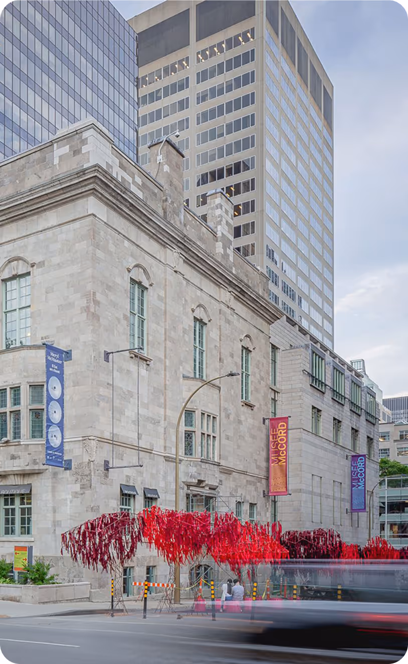 Historic stone building of McCord Museum with red art installation and passing blurred vehicles.