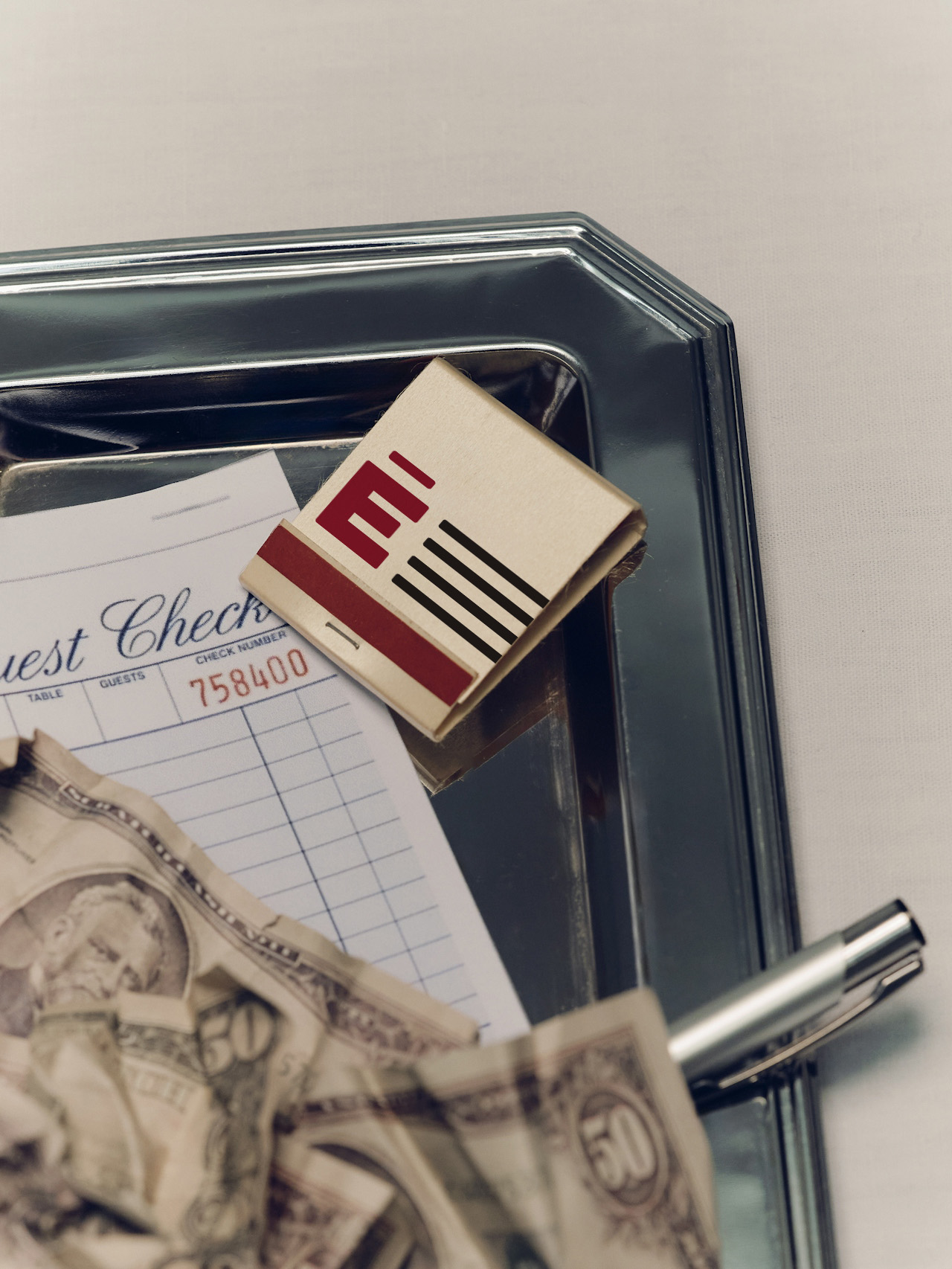 Silver tray with a matchbook, a guest check, a pen, and crumpled cash. Credit: Fanette_Guilloud