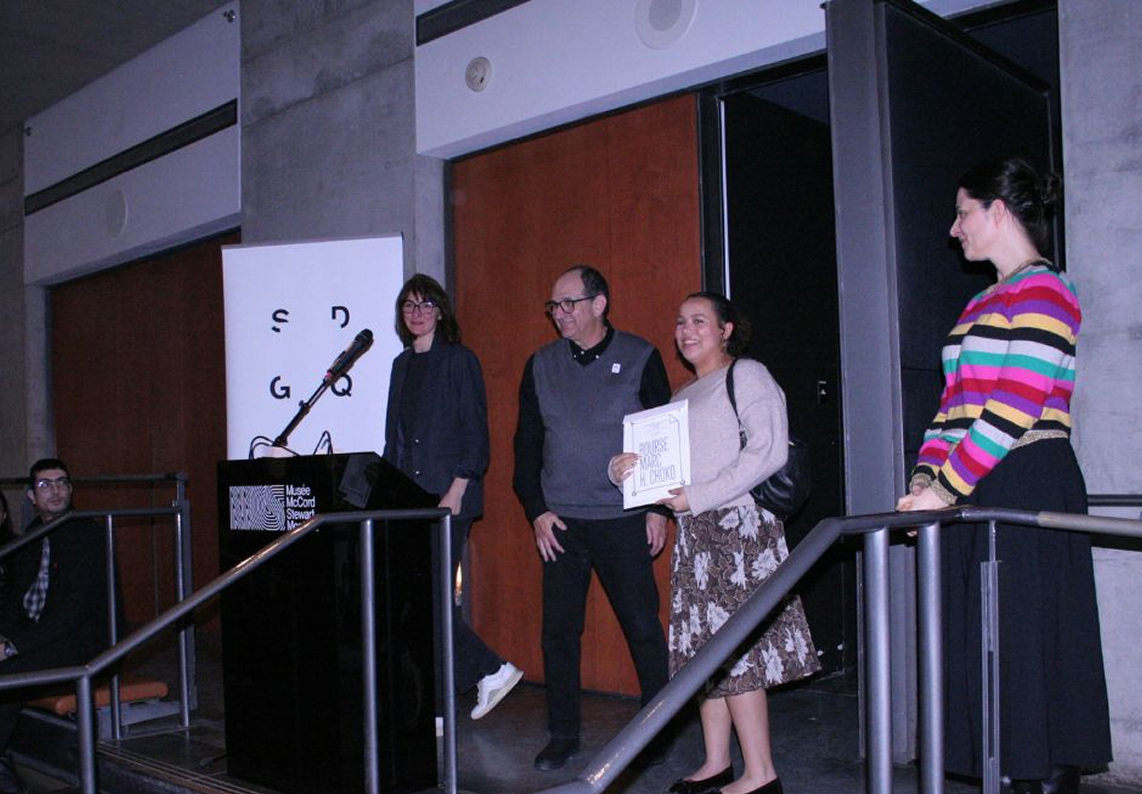 Four people standing near a podium in an indoor venue, one woman holds a certificate and smiles. May-Lee winning 2nd place at the Mark H. Choko poster contest