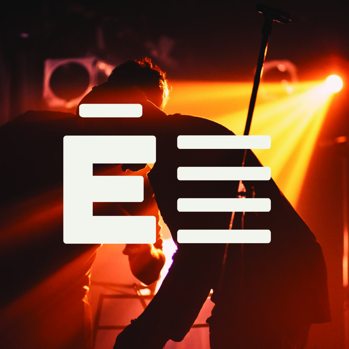 Silhouettes of two people on stage with orange spotlight and a microphone stand in the background. Credit: May-Lee Abel and unsplash