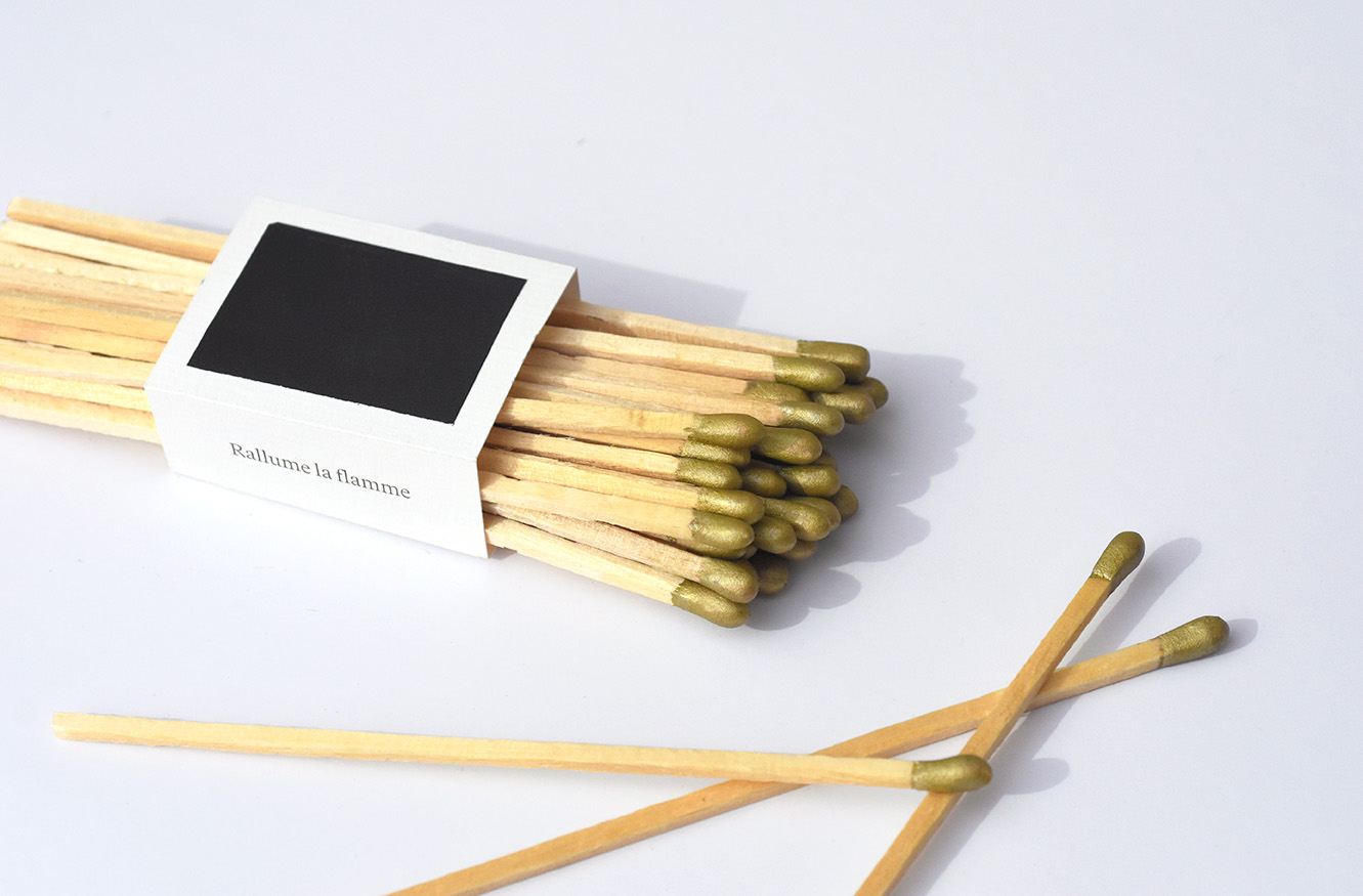 A bundle of wooden matches with gold tips on a white surface, two matches lying separately. Credit: May-Lee Abel