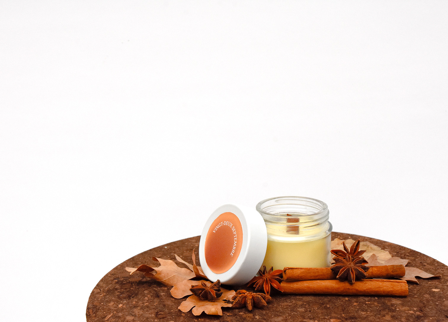 Scented candle in glass jar with spices and dried leaves on round cork mat. Credit: May-Lee Abel