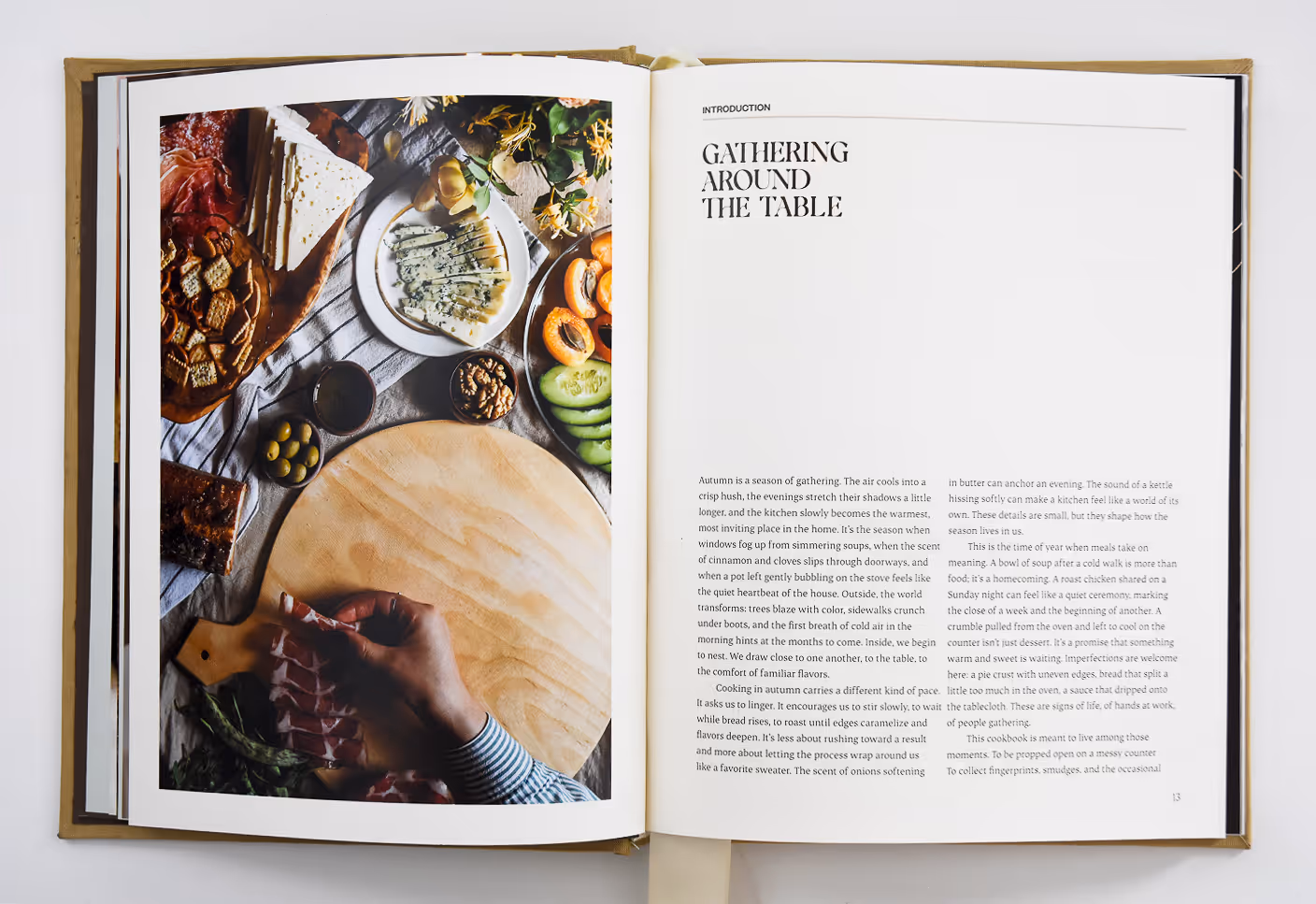 Open cookbook spread showing a picnic board setup and a page titled 'Gathering Around the Table' with introduction text. Credit: May-Lee Abel