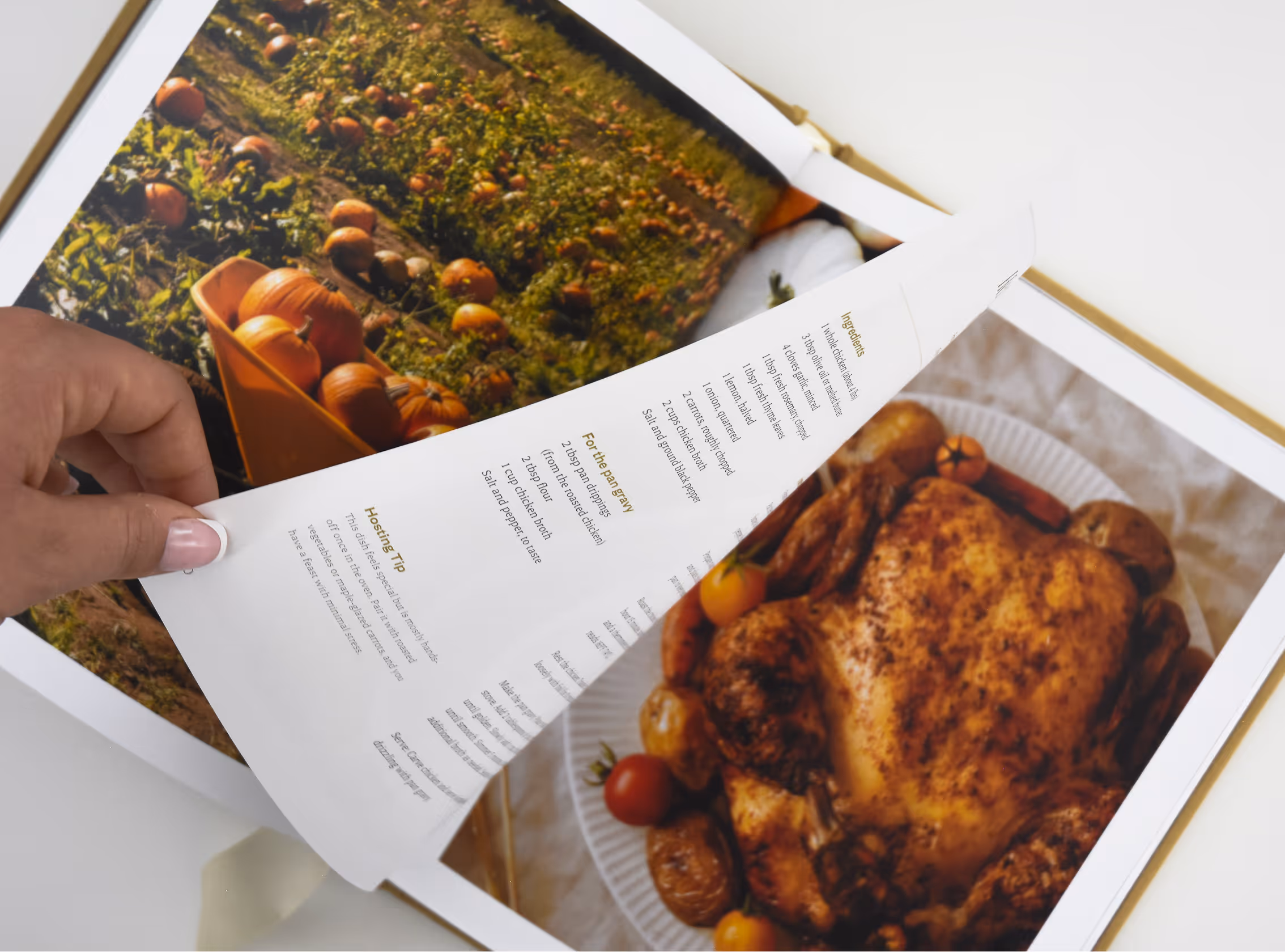 Hand flipping a cookbook page showing a roasted chicken recipe with pumpkins in a field photo. Credit: May-Lee Abel