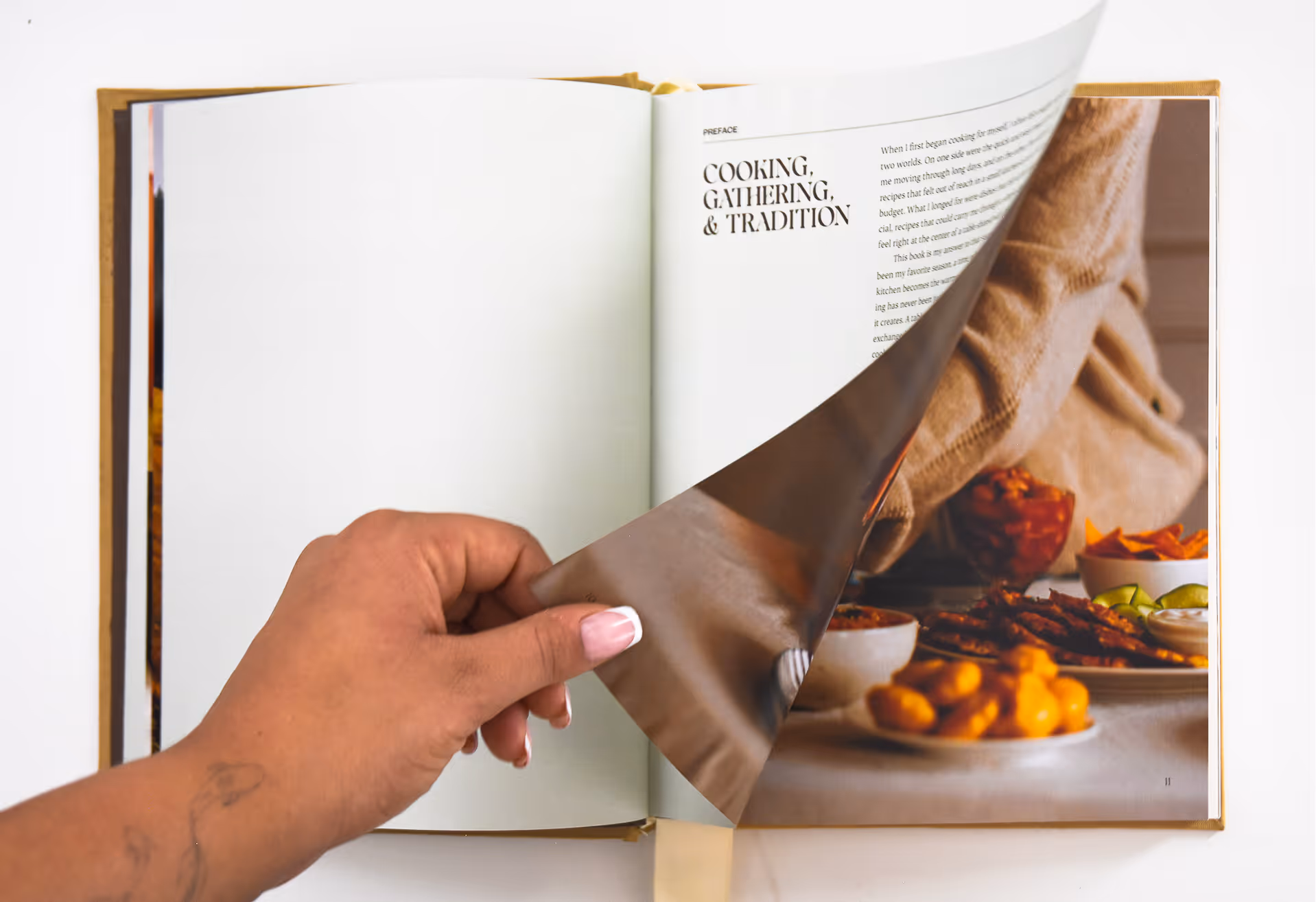 Hand turning a page of a cookbook open to a section titled Cooking, Gathering, & Tradition. Credit: May-Lee Abel