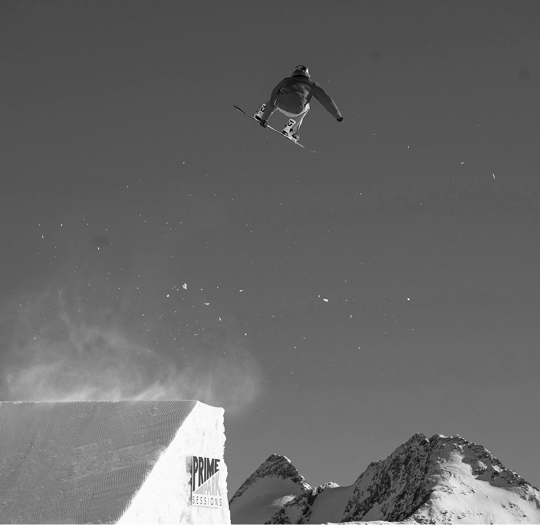 Snowboarder in mid-air above a snowy ramp with mountains in the background. Credit: Unsplash
