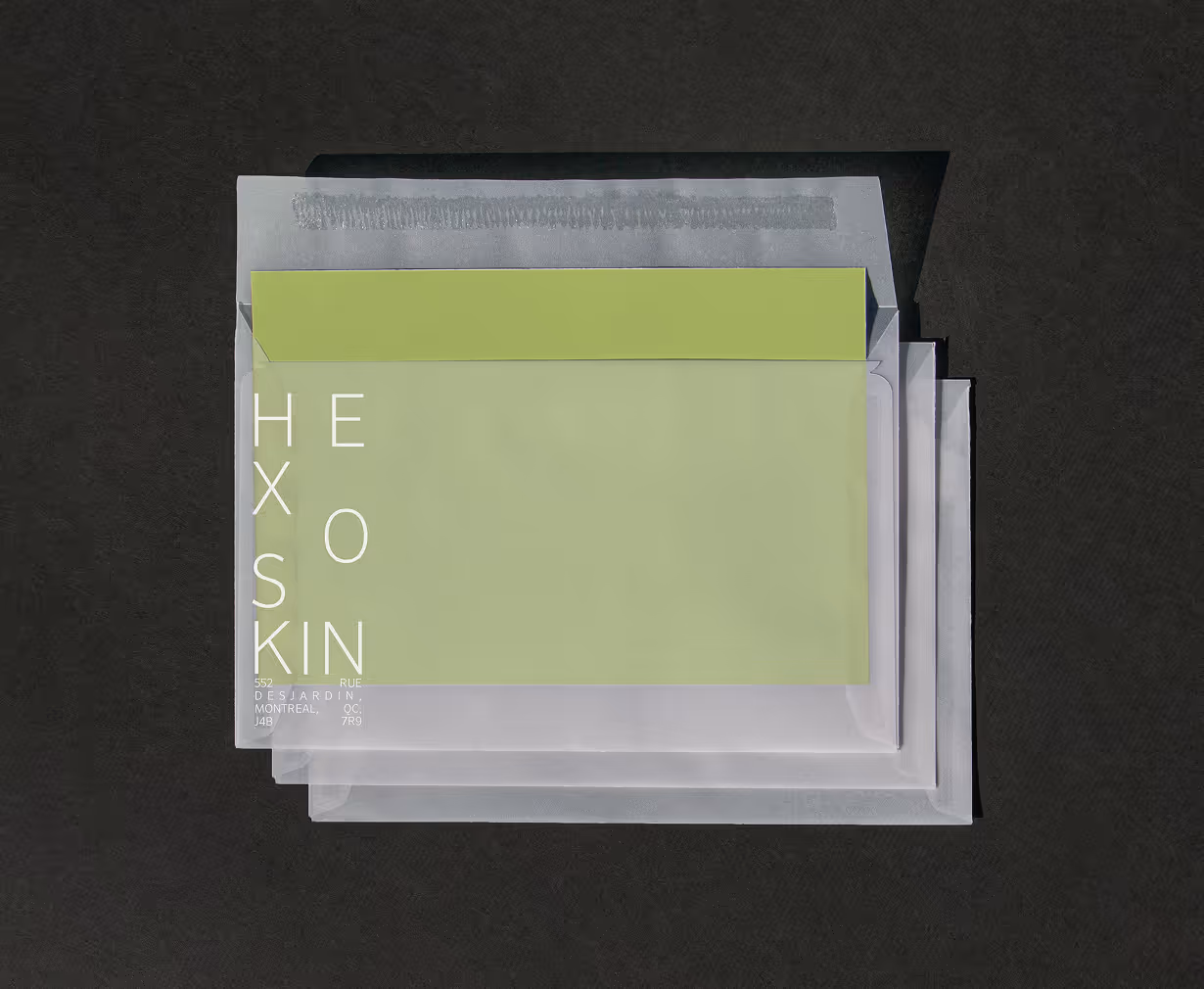Green card partially inside stacked translucent plastic envelopes on a dark textured surface. Credit: May-Lee Abel