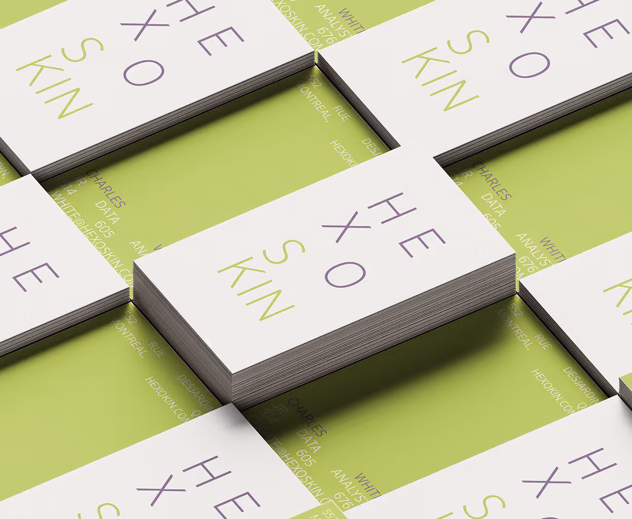 Stacks of white business cards with purple and green text reading HEXOSKIN on a green surface. Credit: May-Lee Abel