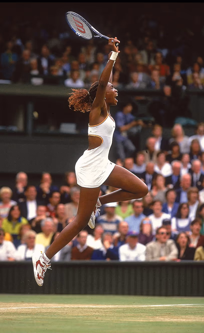 Tennis player in white dress jumps mid-air, celebrating with a racket held high on grass court. Credit: Unsplash