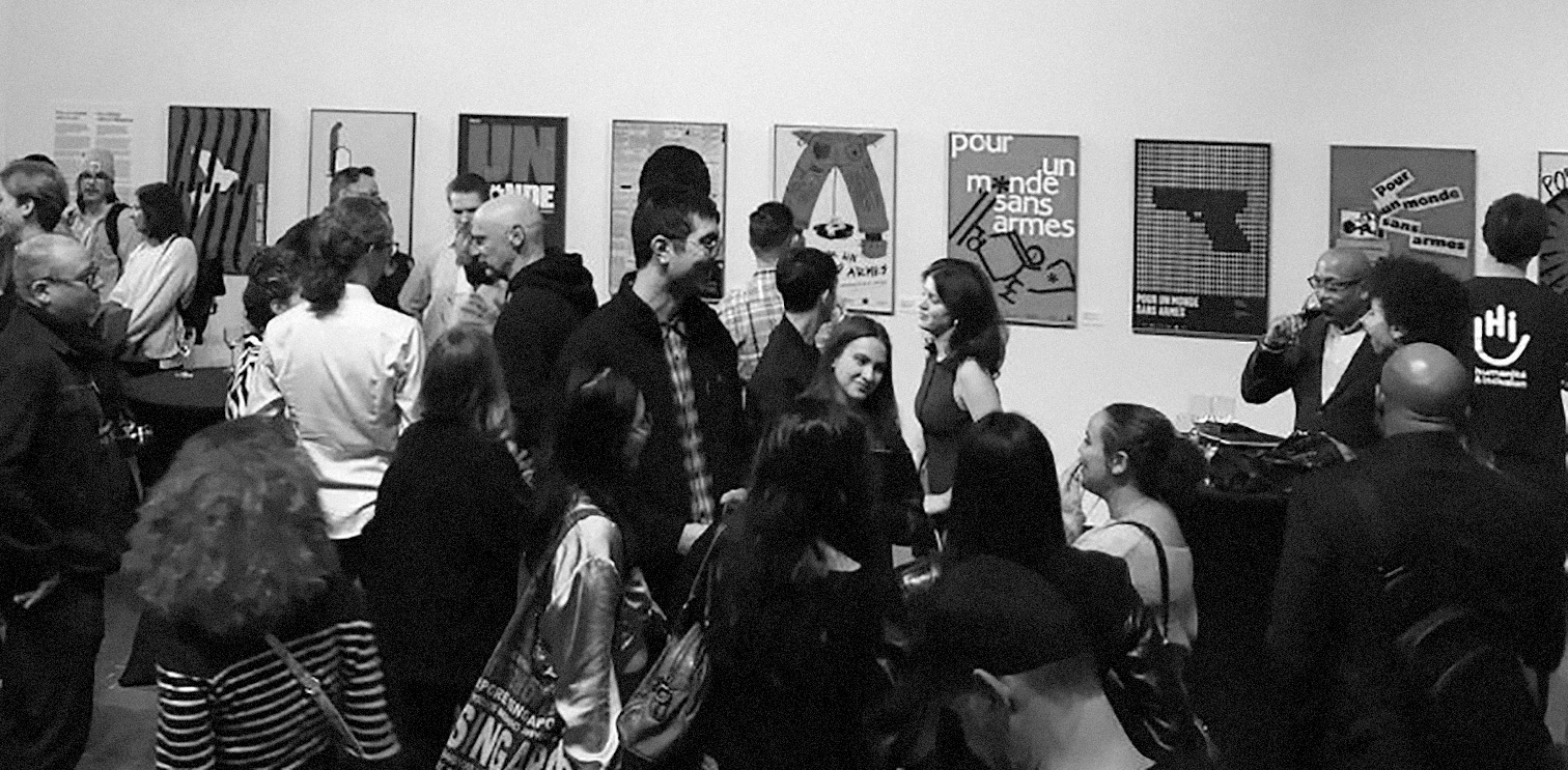 Crowd of people socializing at an art gallery with posters on the wall about a world without arms.