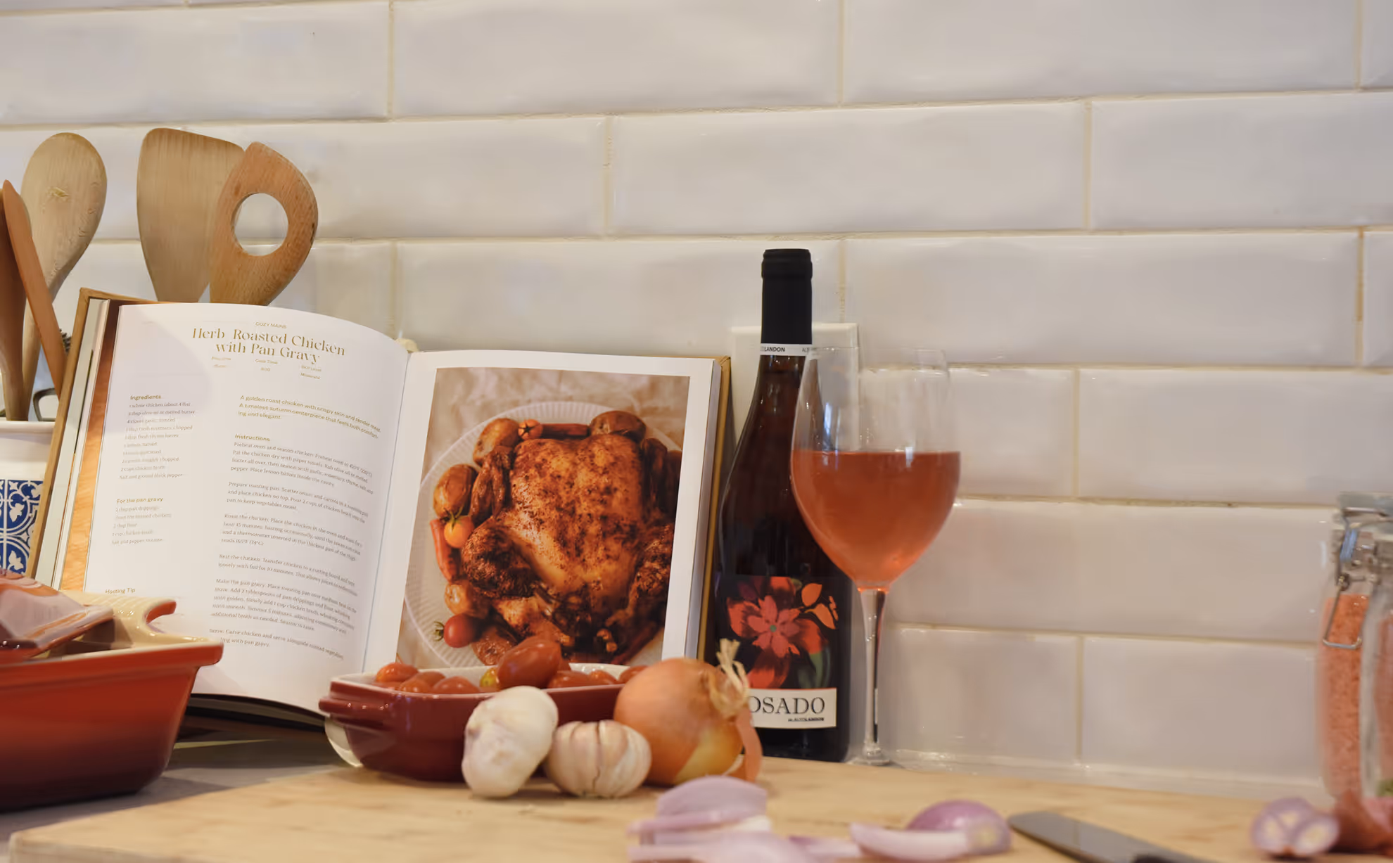 Open cookbook showing herb roasted chicken recipe with ingredients, wine bottle, glass, onion, and garlic on counter. Credit: May-Lee Abel