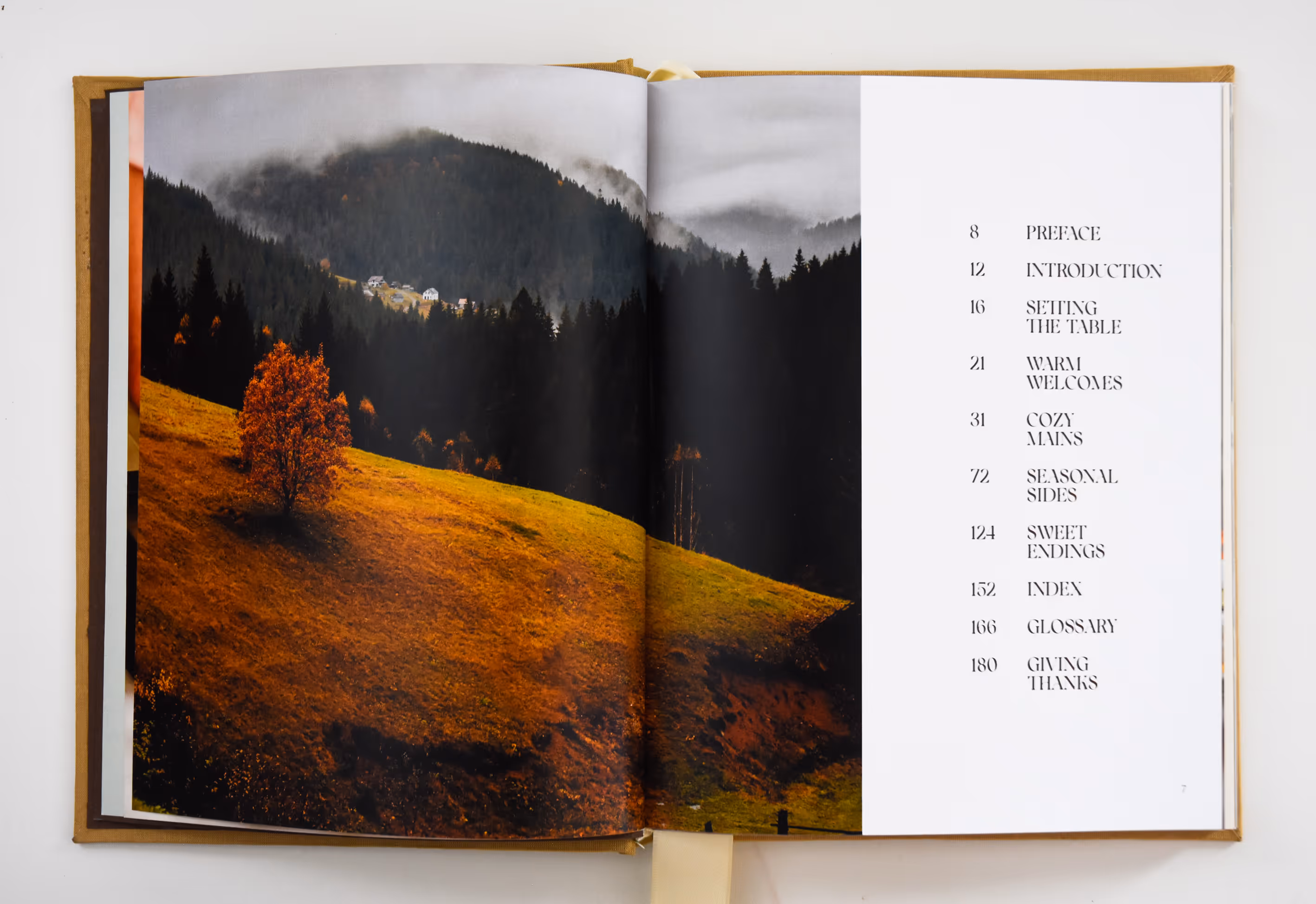 Open cookbook showing autumn landscape photo on left and table of contents on right. Credit: May-Lee Abel