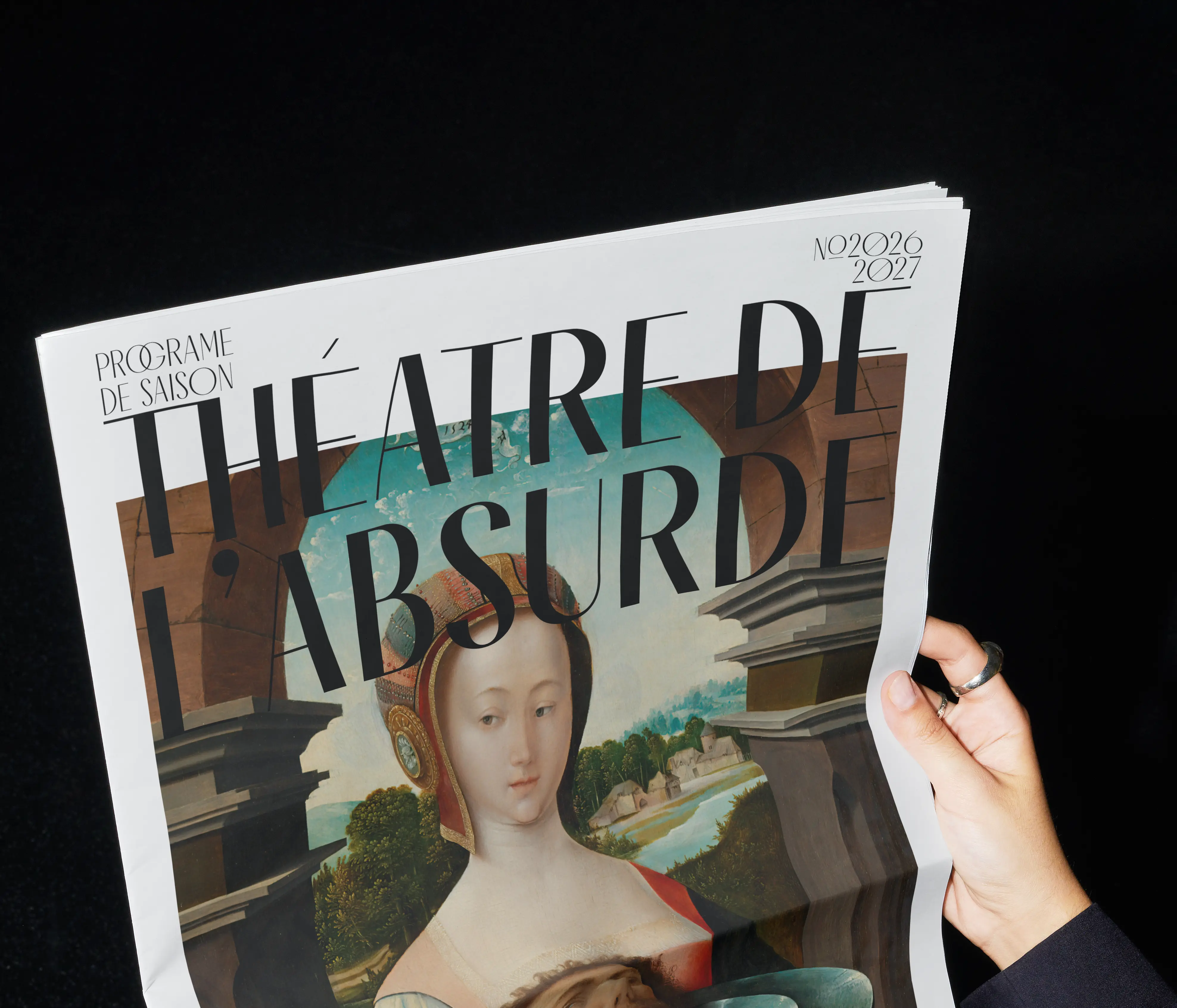 Hand holding a French newspaper titled Théâtre de l'Absurde with a Renaissance-style portrait on cover.