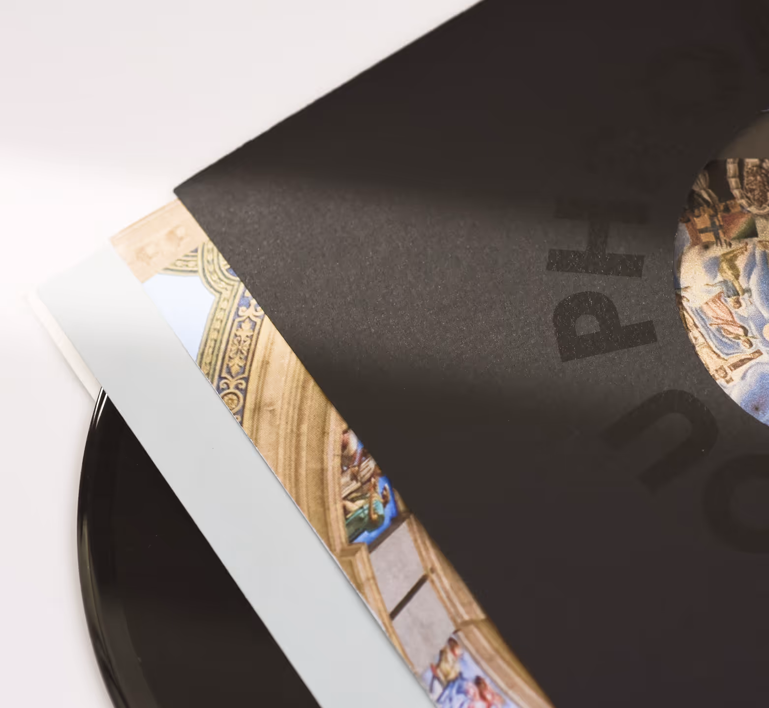 Vinyl record partially covered by two album covers, one black with partial text and one with artistic design. Credit: May-Lee Abel