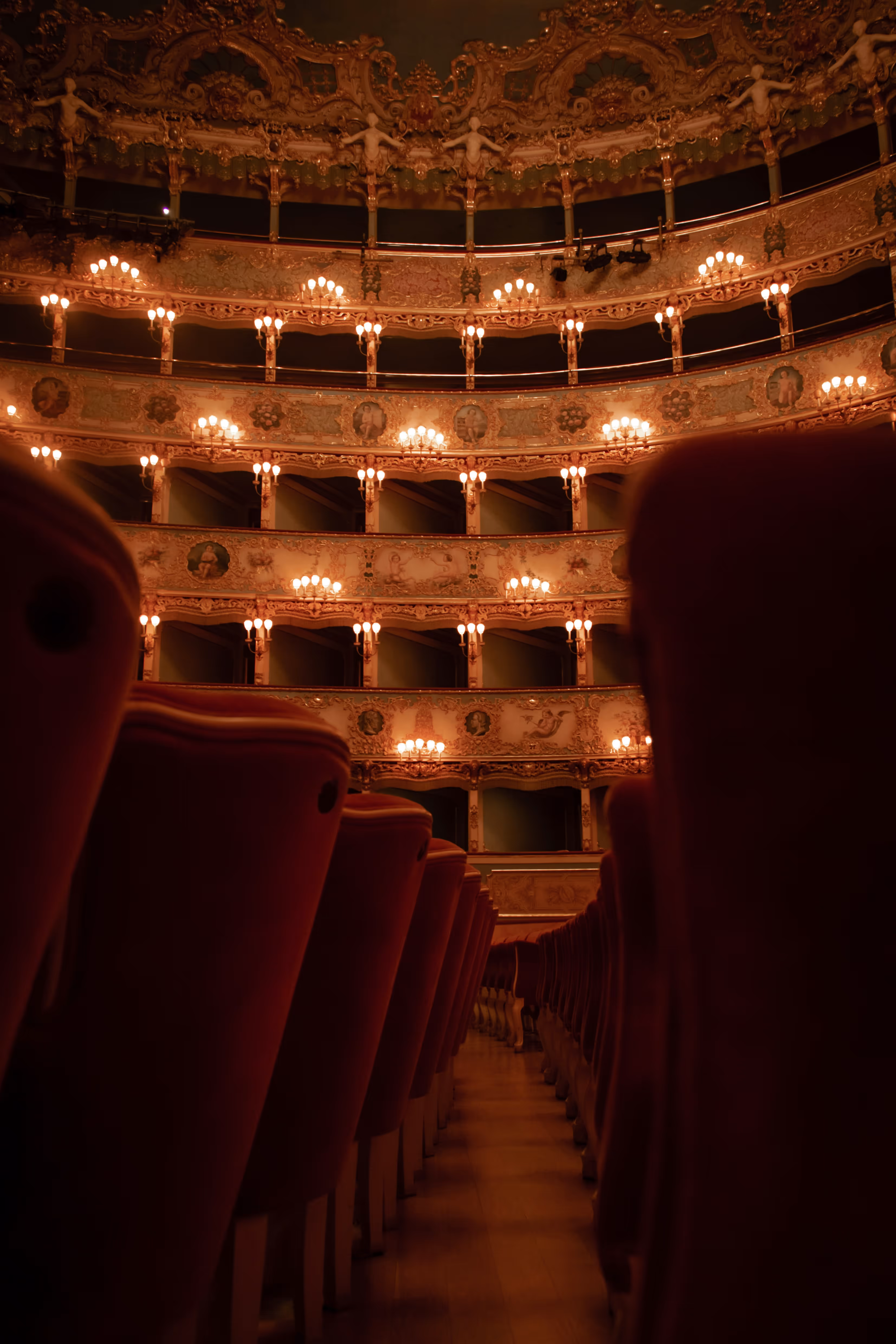 Interior view of an ornate theater with red seats and multiple lit balconies with decorative designs. Credit: Guisi Borrasi