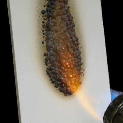 Intumescent fire-resistant coating actively resisting flames on a panel — protecting eaves, decks, and wood siding.