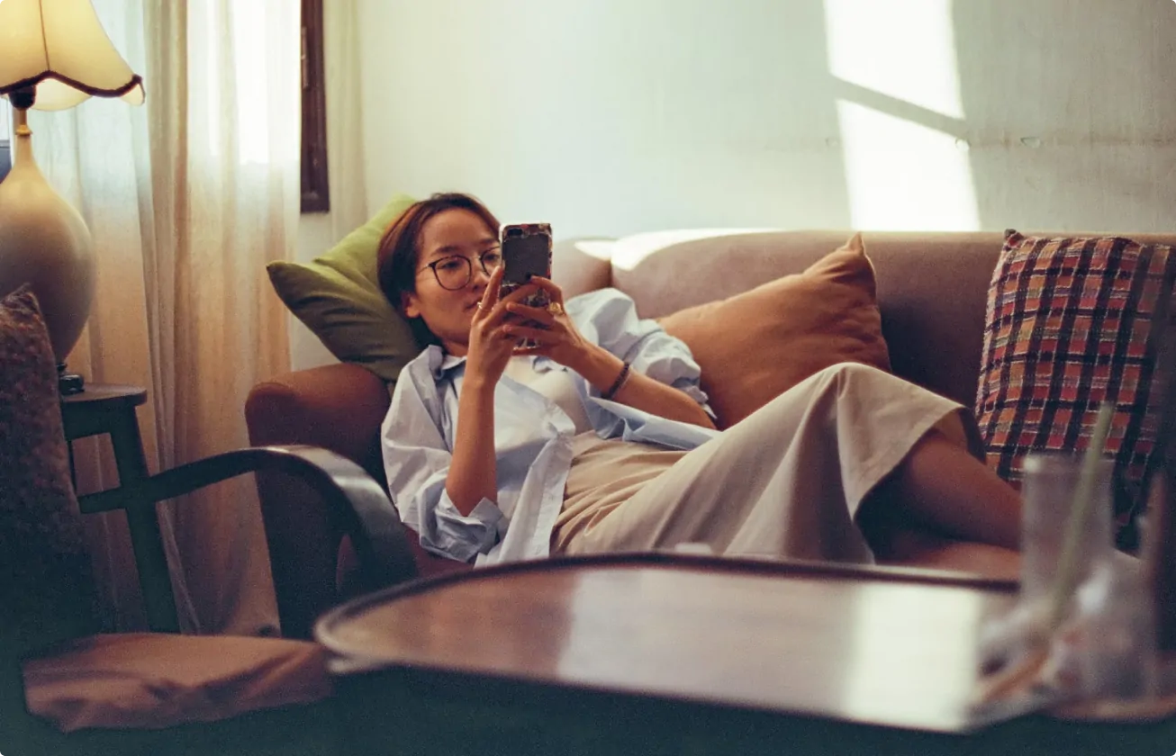 Woman wearing glasses reclining on a couch and looking at her smartphone.