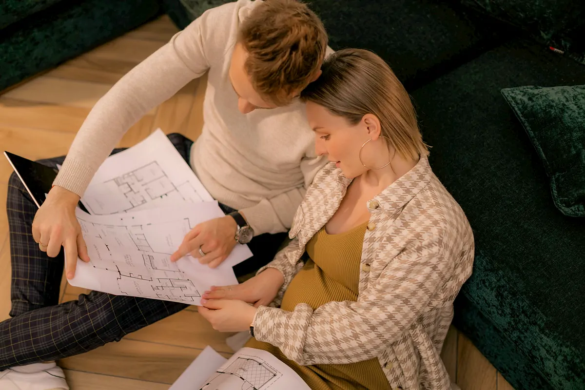 Couple sitting on the floor closely examining and discussing multiple architectural blueprints.
