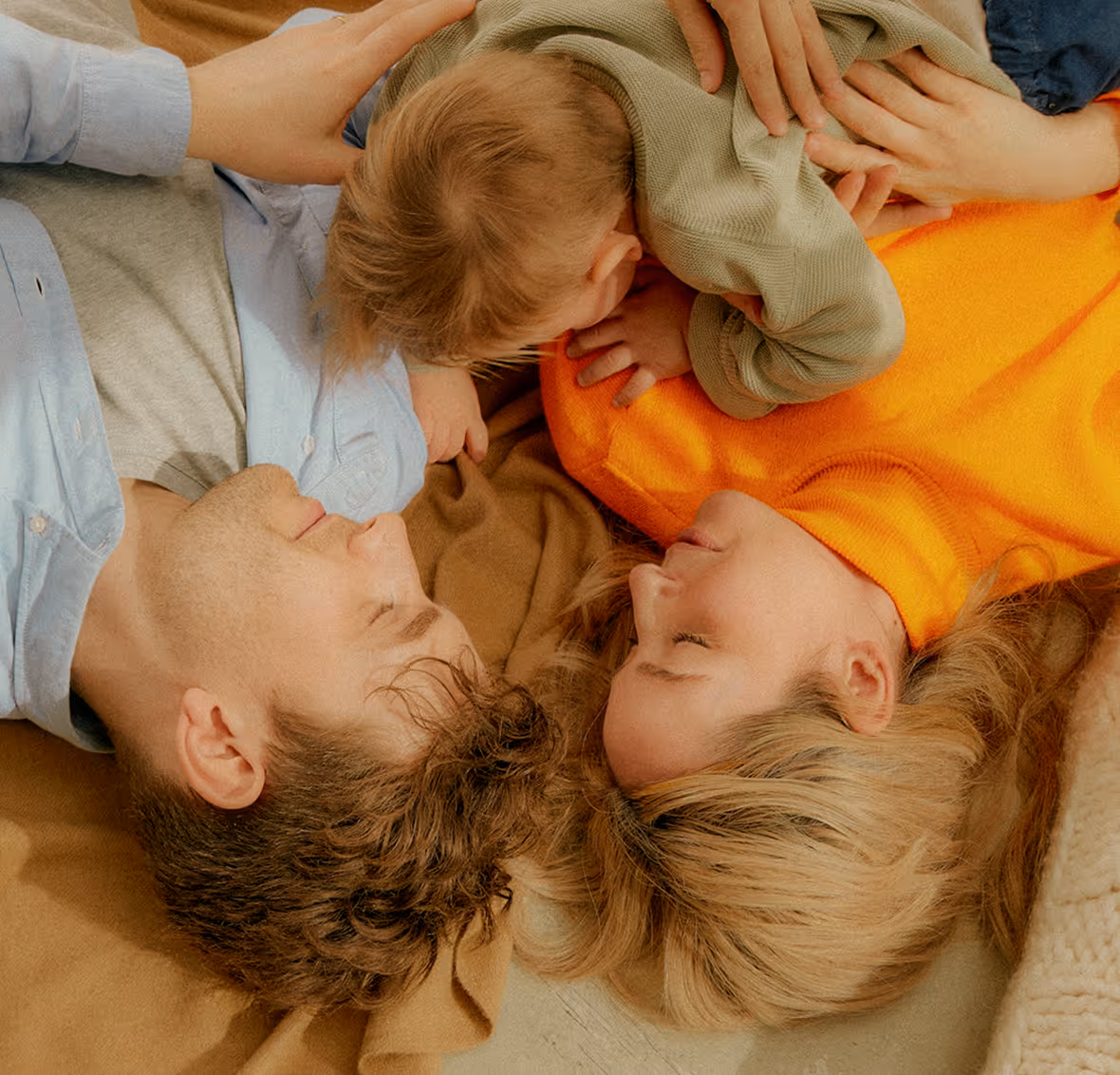 Family lying on a blanket, parents facing each other with their child between them.