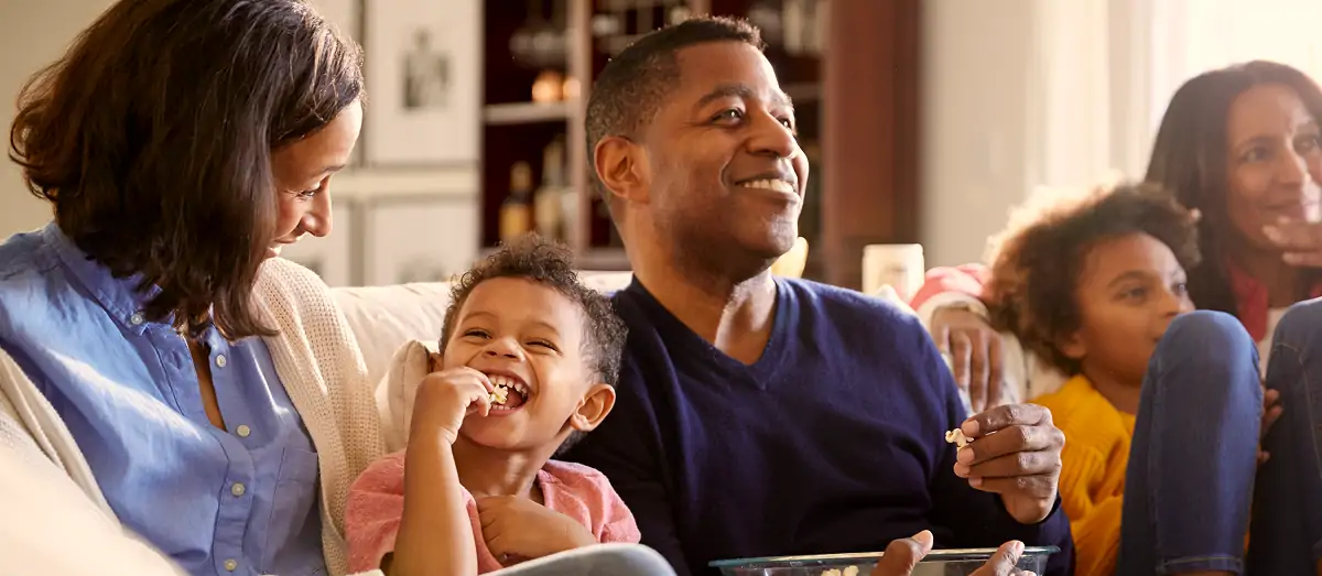 Smiling family sitting on a couch eating popcorn and enjoying time together indoors.