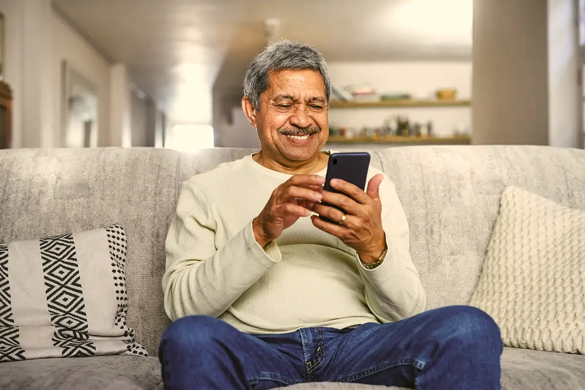 Smiling middle-aged man sitting on a couch using a smartphone.