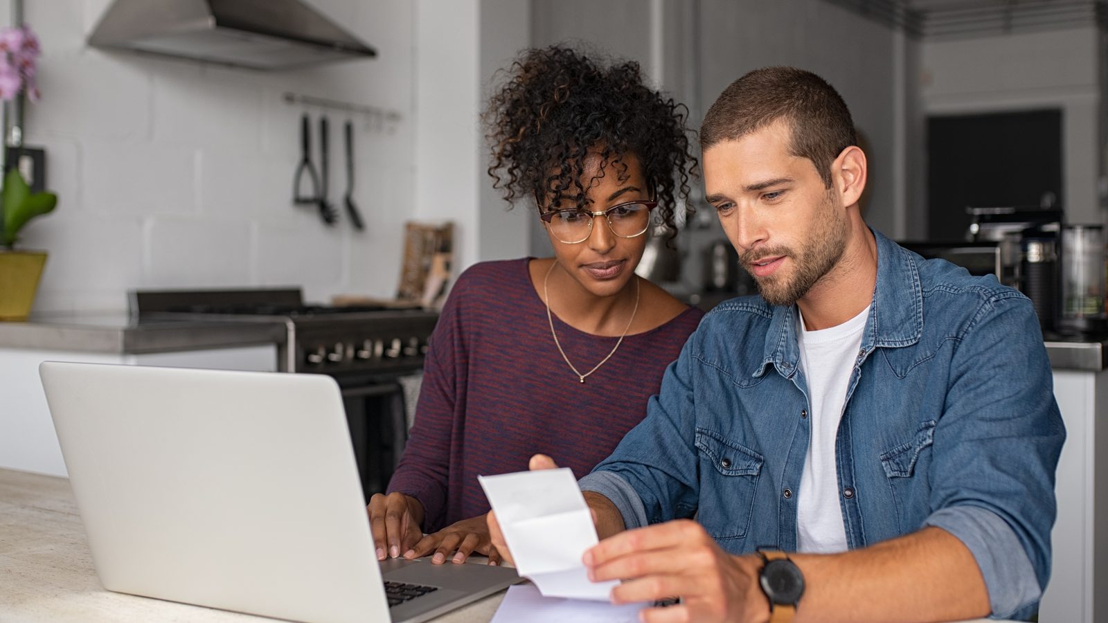Couple reviewing paperwork beside a laptop at a kitchen counter