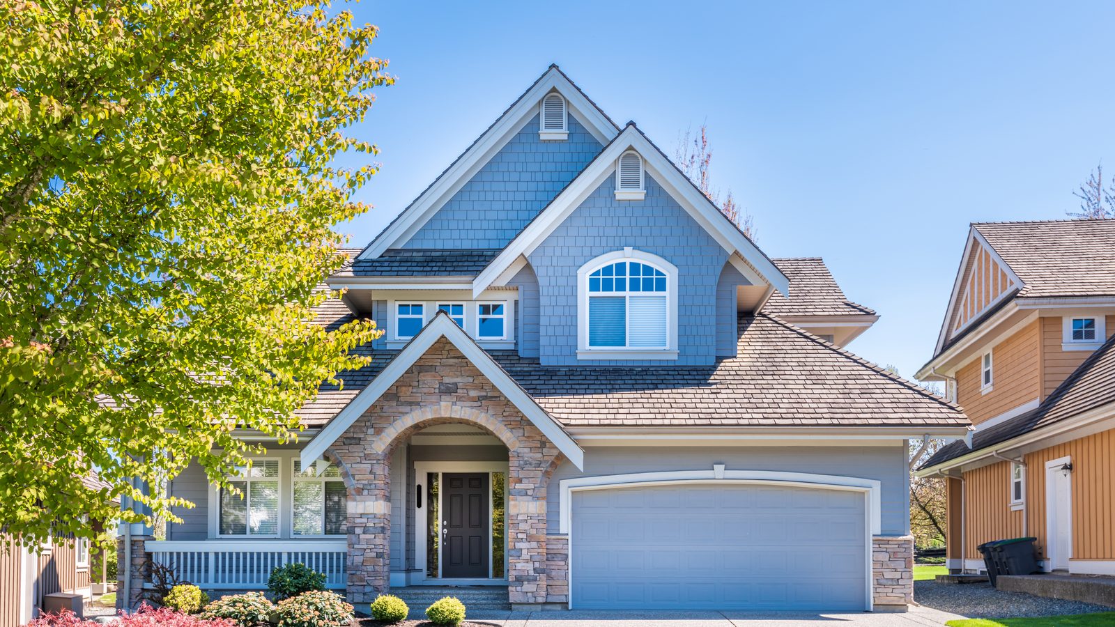Blue two story suburban home with an attached garage and landscaped front yard