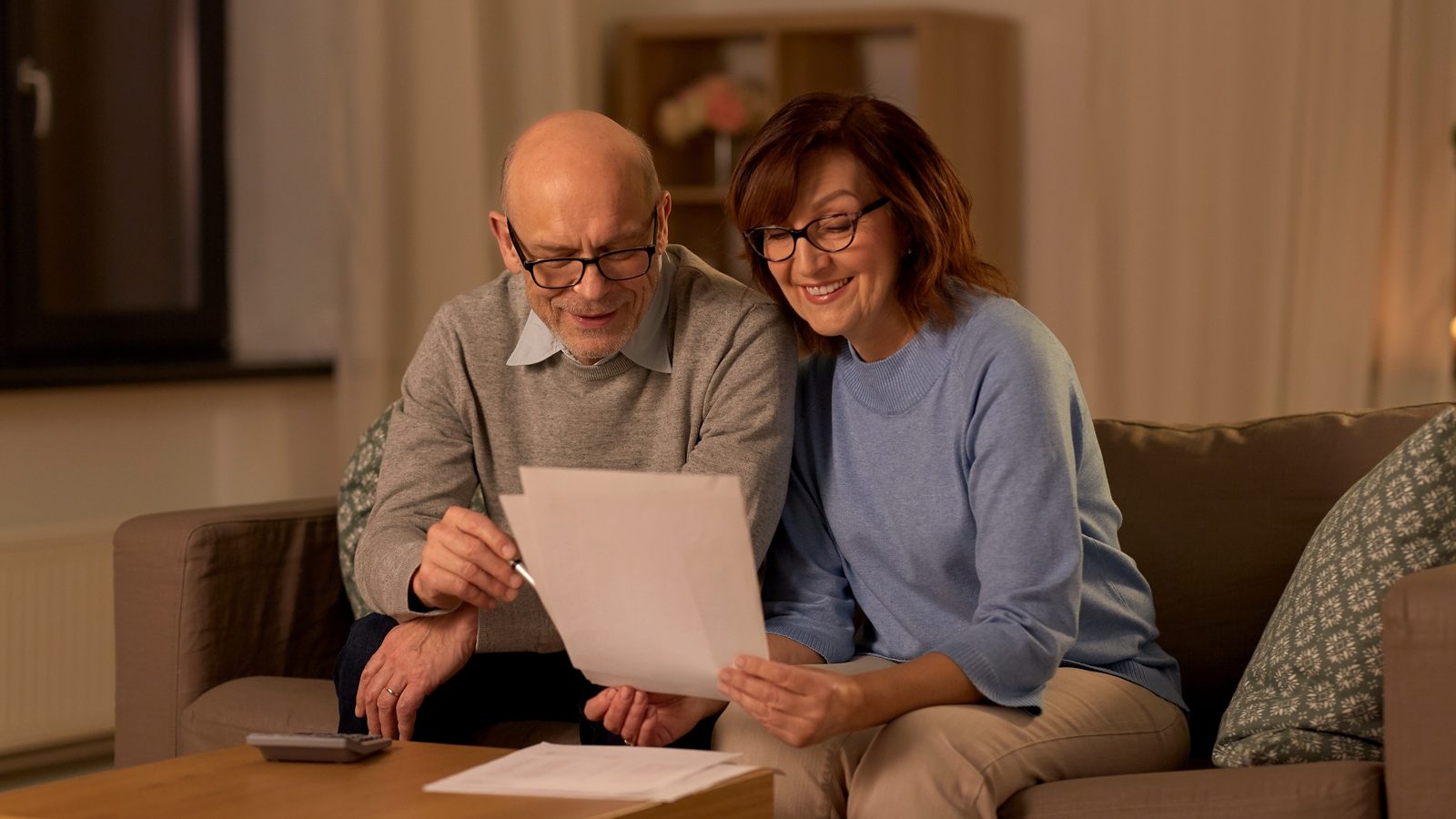 Older couple reviewing paperwork with a calculator nearby at home