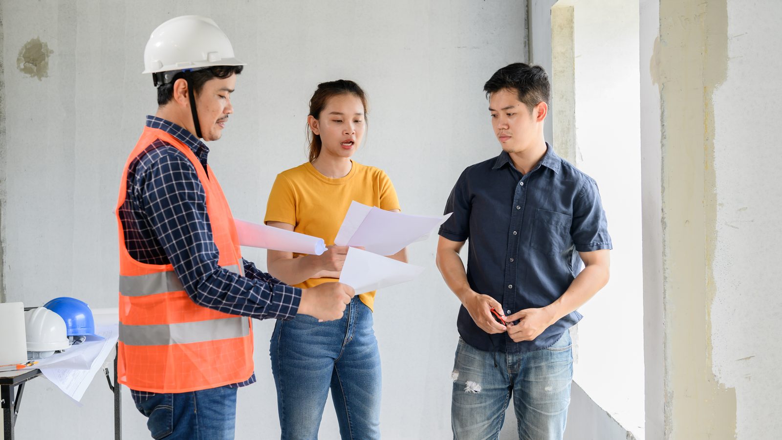 Couple reviewing plans with a contractor inside an unfinished room