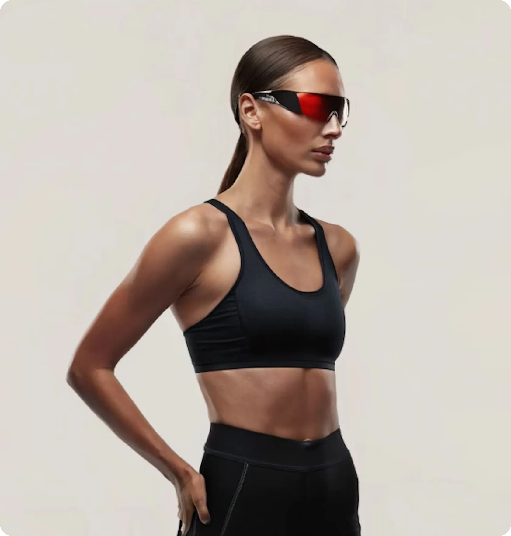 Athletic woman in black sportswear and red-tinted sports sunglasses, standing sideways with hands on hips.