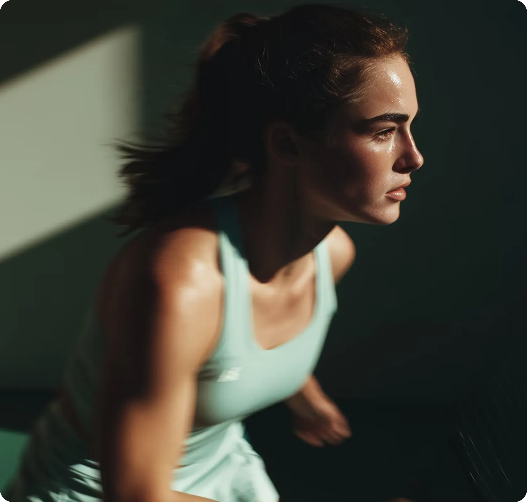 Focused woman in athletic wear with ponytail, perspiring and preparing to play tennis in dramatic lighting.