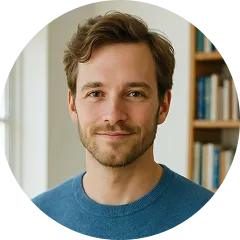 Smiling man with short brown hair and beard, wearing a blue shirt, in front of a bookshelf.
