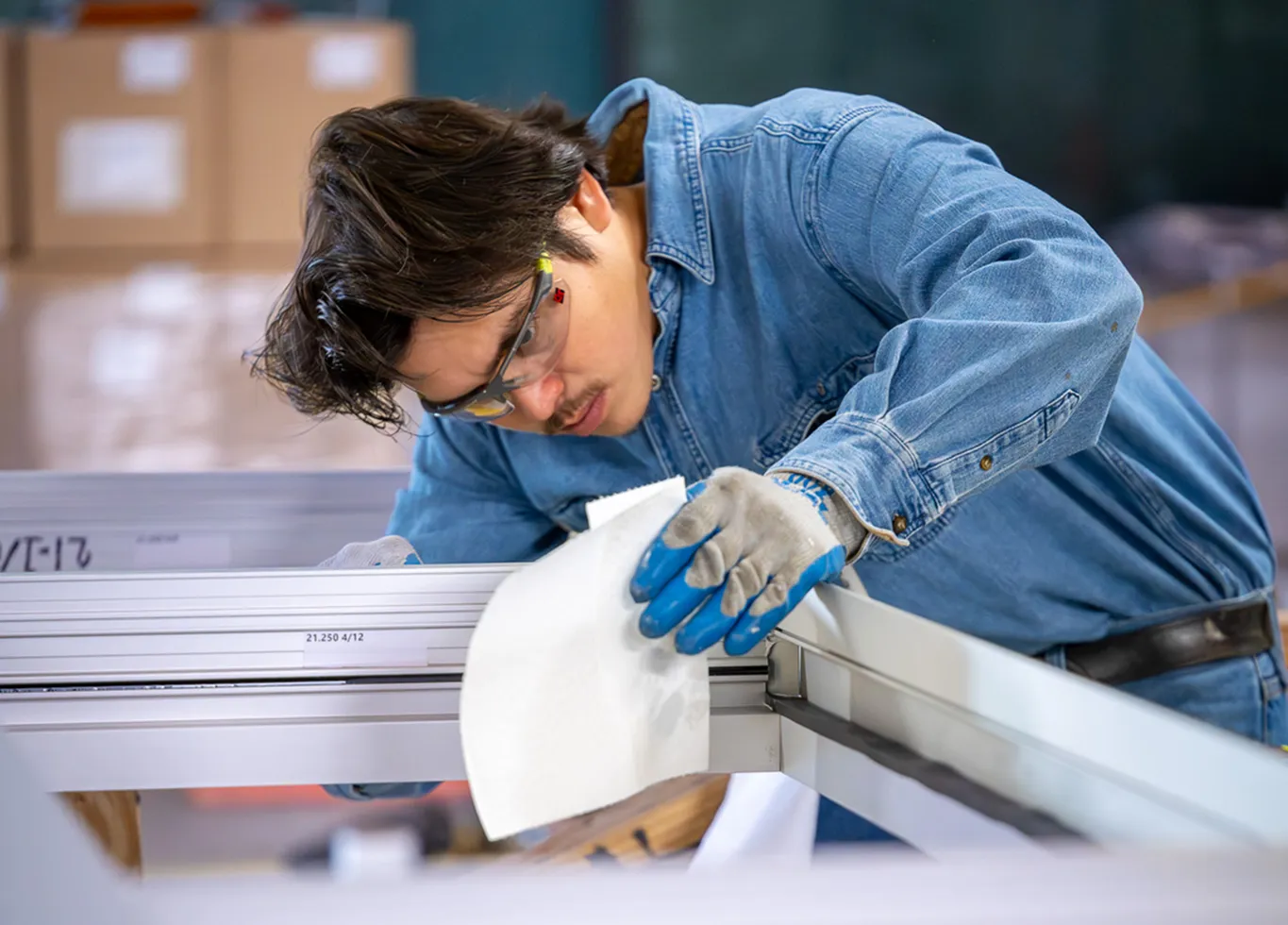 A BrightLeaf Glass & Metal technician in safety glasses and work gloves carefully inspecting an aluminum frame at the company's Smithfield fabrication facility