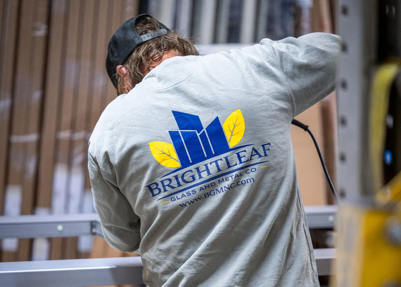 A BrightLeaf Glass and Metal Co. crew member working at the Smithfield fabrication facility, wearing a branded company sweatshirt featuring the BrightLeaf logo