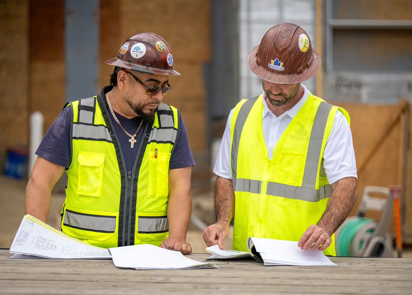 A BrightLeaf Glass and Metal project manager and site foreman reviewing construction blueprints and plans together at an active commercial job site in North Carolina