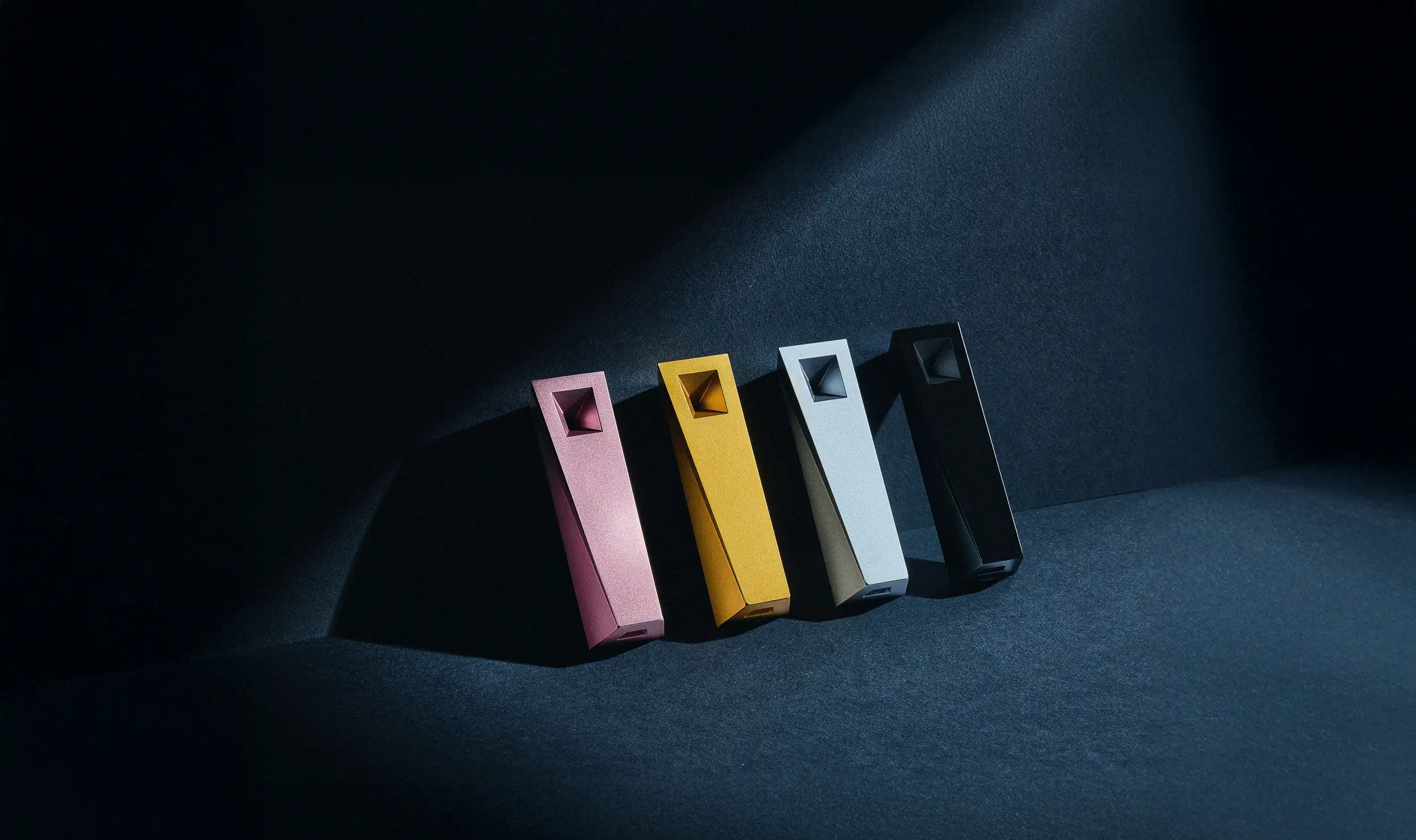 Tempest magnetic cooling pipe collection in pink Glimmer, gold Radiance, silver Mercury, and black Abyss arranged diagonally on a dark textured surface with dramatic directional lighting