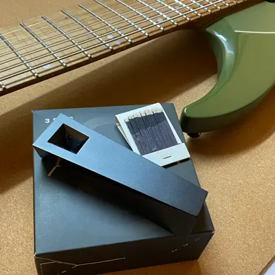 Black Abyss Tempest pipe resting on box beside guitar neck and matchbook on warm surface