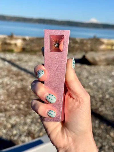 Woman's hand holds the Pink Tempest pipe outdoors showing geometric bowl design and anodized aluminum finish