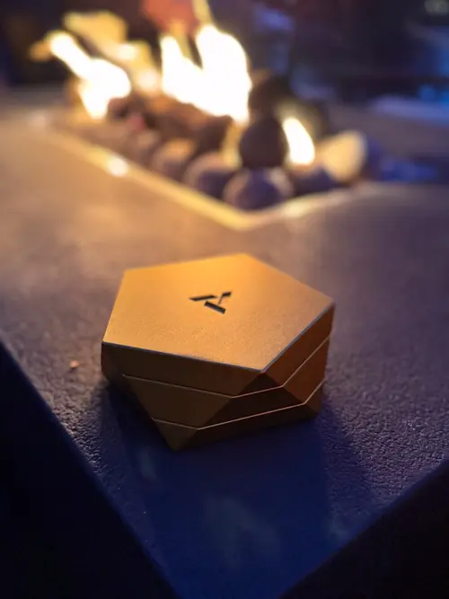 Gold Vesta magnetic vessel on outdoor table with fire pit flames blurred in background