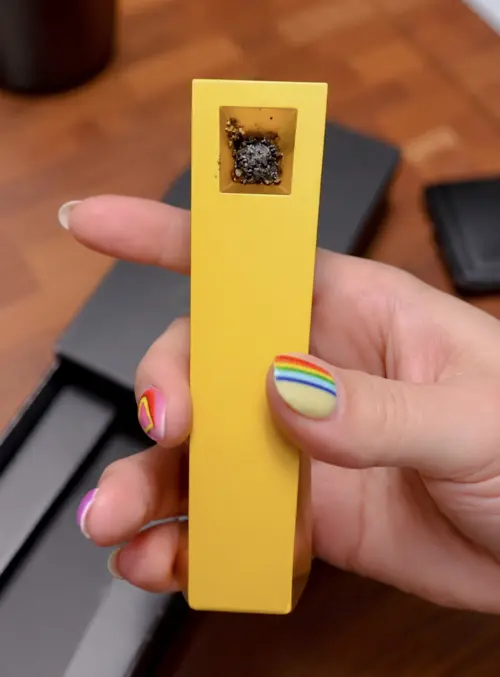 Gold Radiance Tempest pipe held in hand with rainbow-painted nails and used bowl indoors
