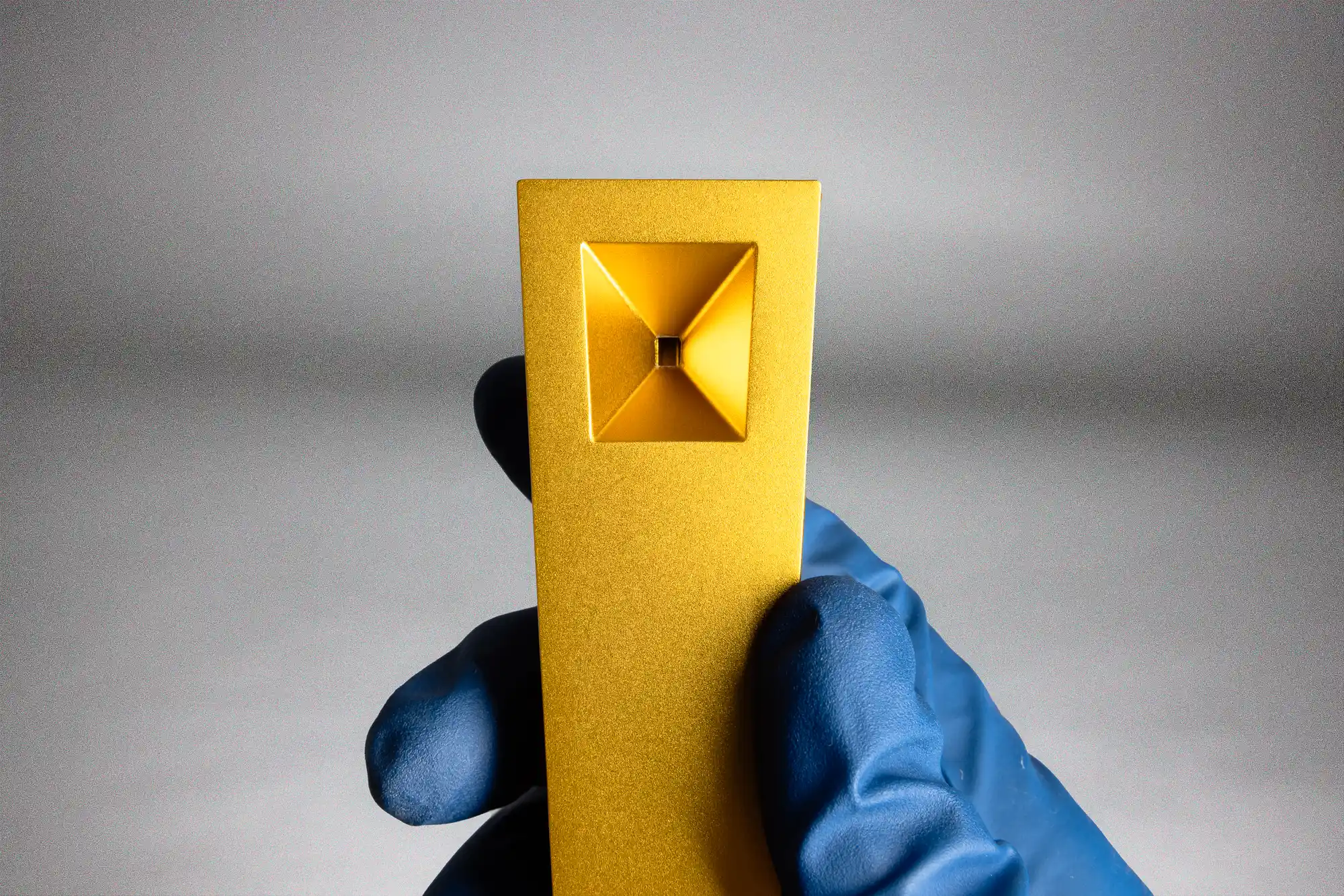 Gold Tempest Radiance magnetic pipe held in blue glove showing clean square bowl and anodized aluminum finish