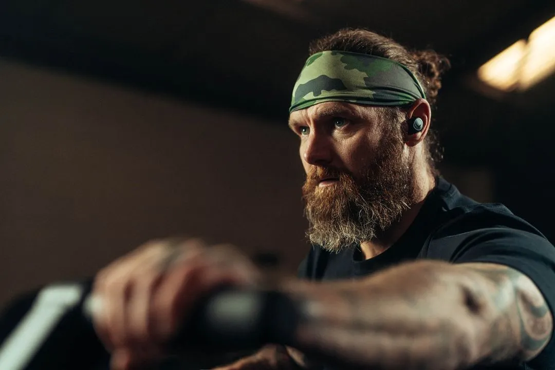 A man with a beard and a headband cycling on a machine.