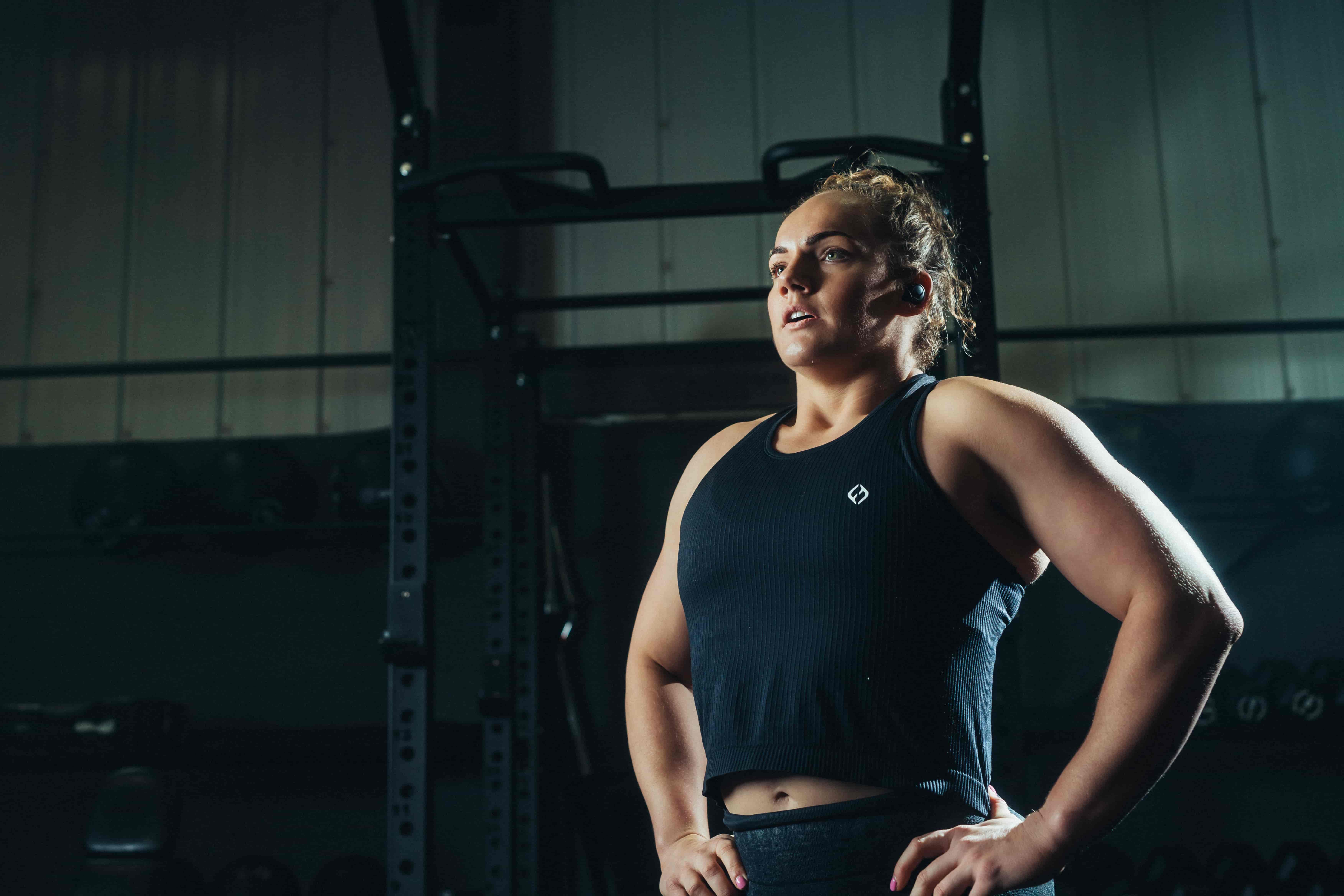 Athlete wearing phone-free workout earbuds during a gym training session, standing with hands on hips between sets