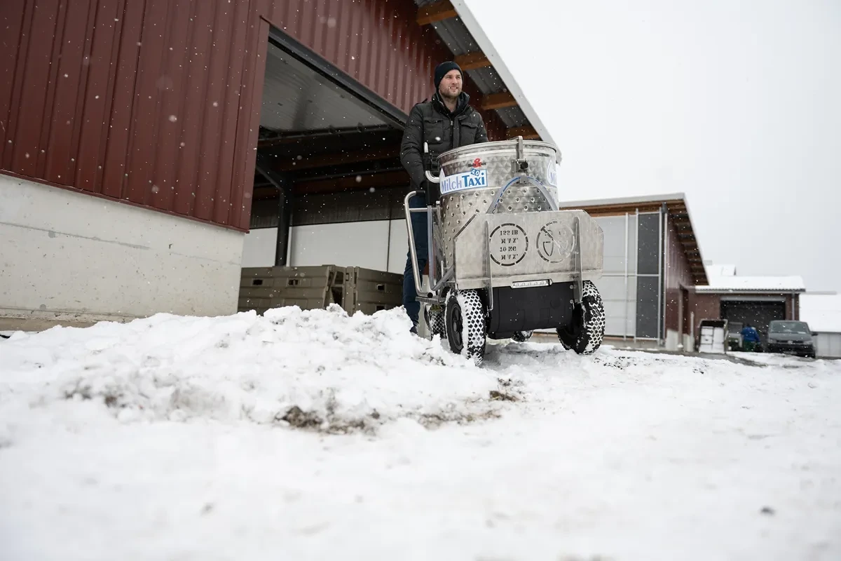 Ošetřovatel s vozíkem MilkTaxi na zasněženém dvoře farmy