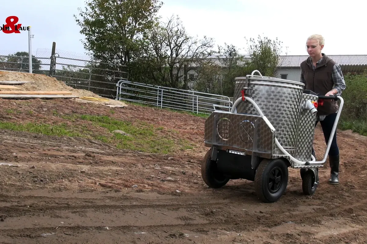 Ošetřovatel tlačí vozík MilkTaxi po venkovní ploše farmy