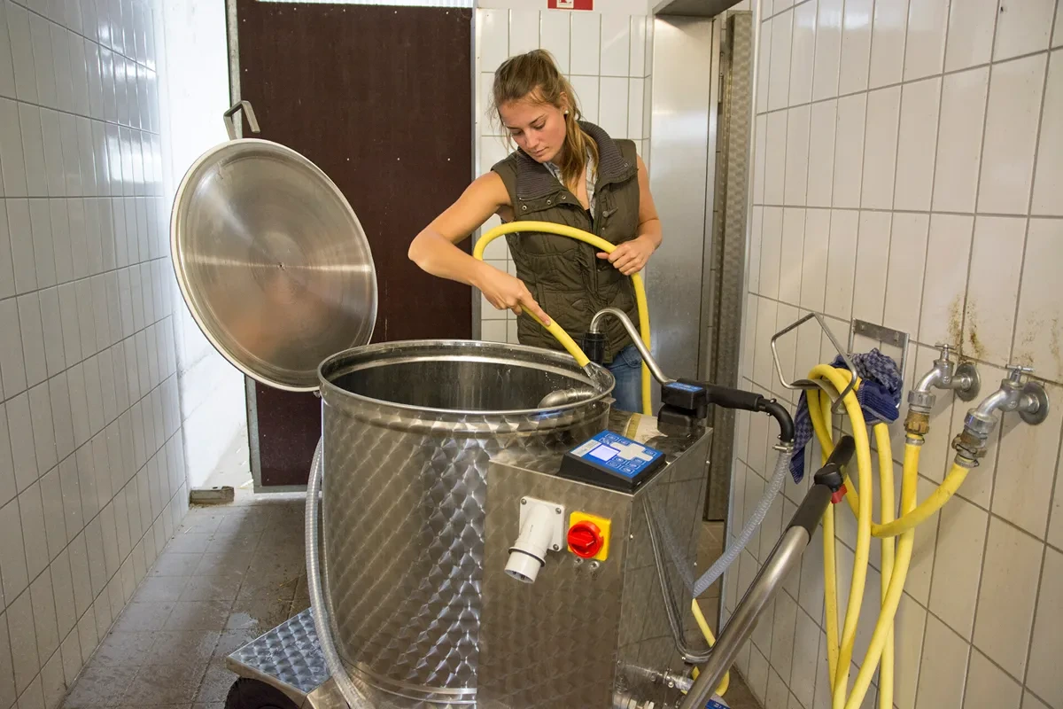 Ošetřovatelka čistí nádobu vozíku MilkTaxi hadicí