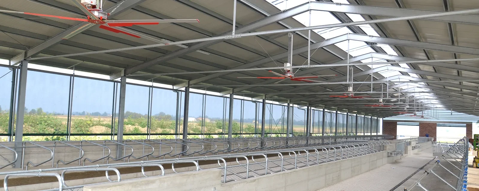 Řada stropních ventilátorů pod střechou prosvětlené stáje