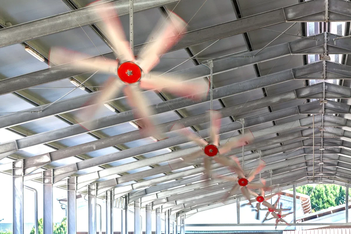 Tři vertikální ventilátory v pohybu pod stropem stáje