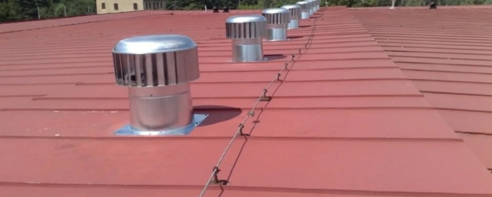 Řada ventilačních turbín na červené plechové střeše zemědělského objektu