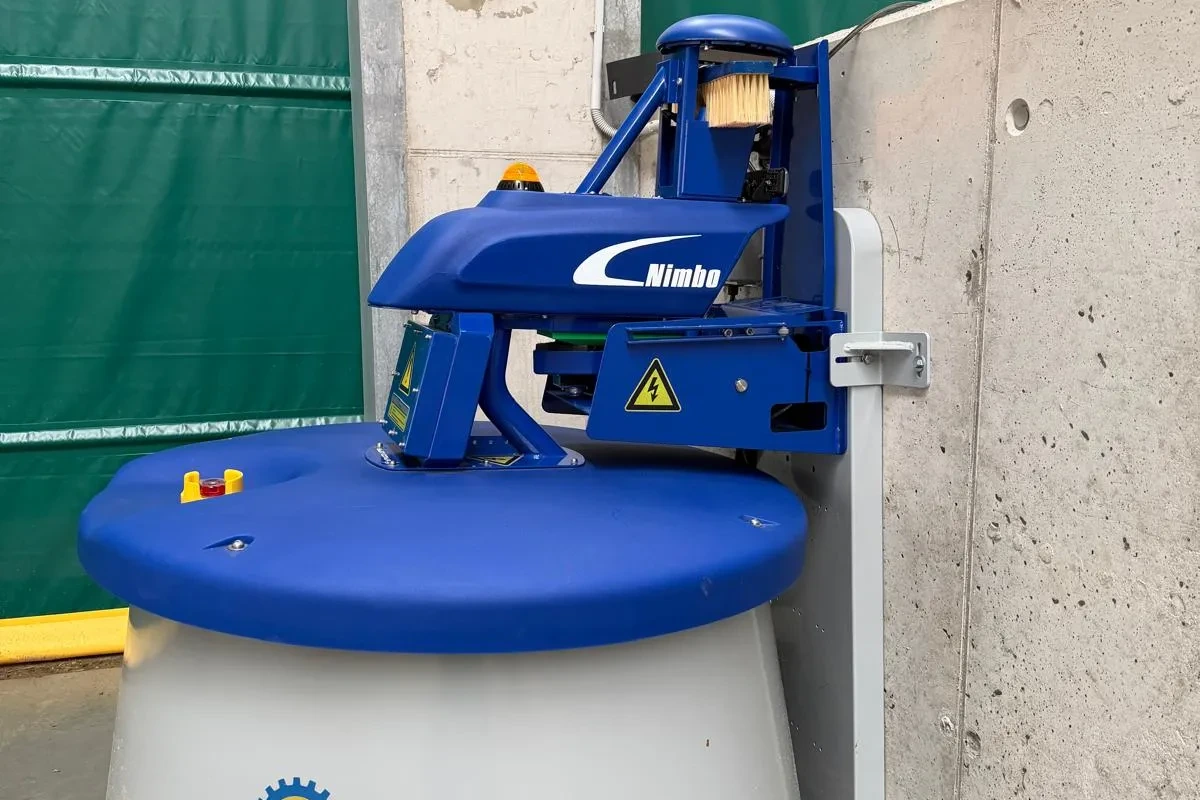 Robot Nimbo zaparkovaný u nabíjecí stanice v rohu stáje